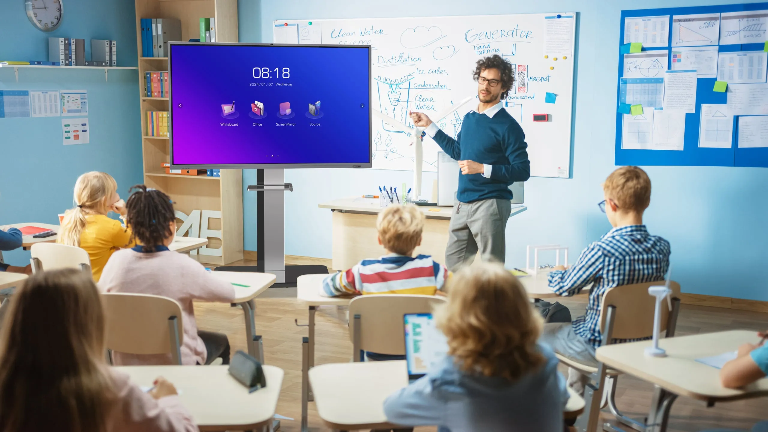 Keng sinfxonada oʻqituvchi Horion interaktiv panelida dars oʻtmoqda, oʻquvchilar partada